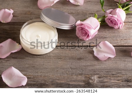 cosmetic cream with pink roses on old wooden table