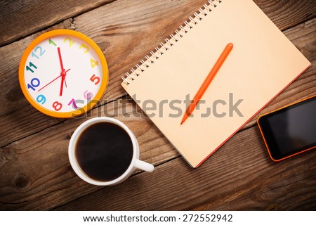 Smart phone, alarm clock, cup of coffee and notebook on wooden background