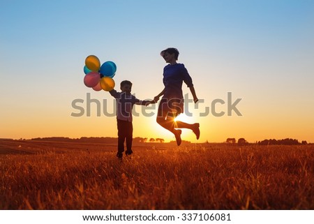 happy mother and son jumping with balloons outdoor