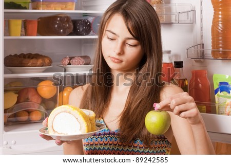 young woman with apple and cake on background fridge