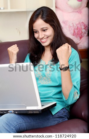Excited Indian woman working with laptop sitting on sofa