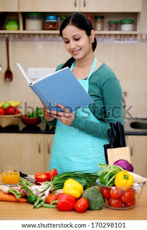 Smiling young woman reading a book in her kitchen