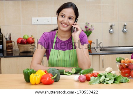 Smiling young woman talking on cellphone in kitchen