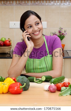 Smiling young woman talking on cellphone in her kitchen