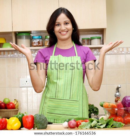 Excited young woman standing with open palms in kitchen