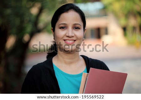 Happy young female student at college campus and carrying books