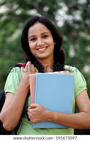 Happy young female student at college campus and carrying books