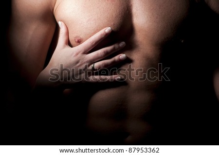 Female hand on the man\'s muscular chest.