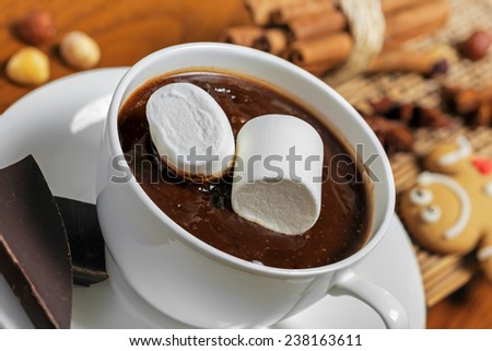 Mug of hot chocolate with marshmallow on table with gingerbread, nuts and cinnamon