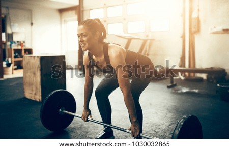 Fit young woman in sportswear smiling while lifting heavy weights during a workout session in a gym