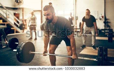 Fit young man in sportswear straining to lift heavy weights during a workout session in a gym