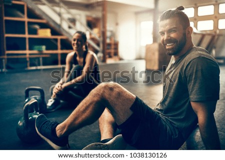 Fit people in exercise gear sitting together on the floor of a gym laughing together after a workout