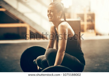 Fit young woman in sportswear smiling while preparing for a workout session with heavy weights in a gym