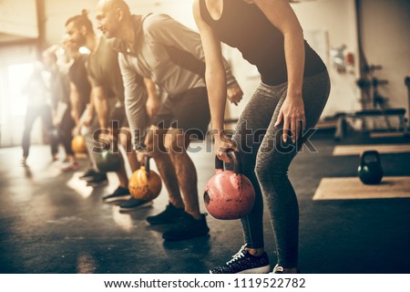 Group of fit people in exercise gear standing in a row lifting dumbbells during an exercise class at the gym