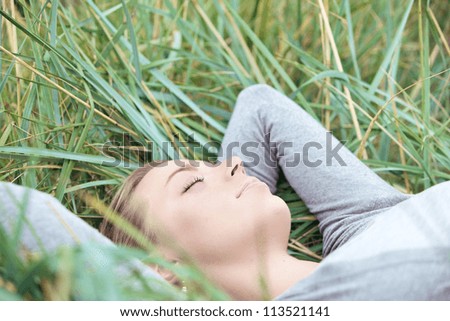 Beautiful young woman with a serene expression lying on her back sleeping in the grass enjoying the outdoor peace and tranquillity