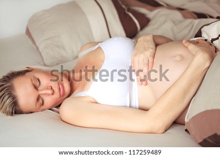 Beautiful heavily pregnant woman sleeping in her bed on her back with her hands folded over her swollen belly