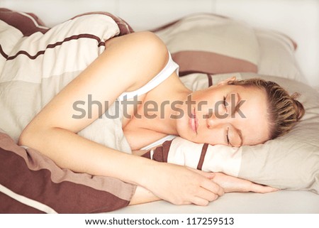 Beautiful blonde woman sleeping peacefully in her bed under her brown patterned duvet with a calm serene expression