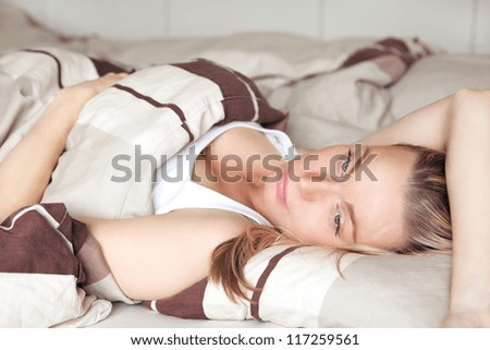 Beautiful young blonde woman lying back on her bed daydreaming as she relaxes having a lazy day