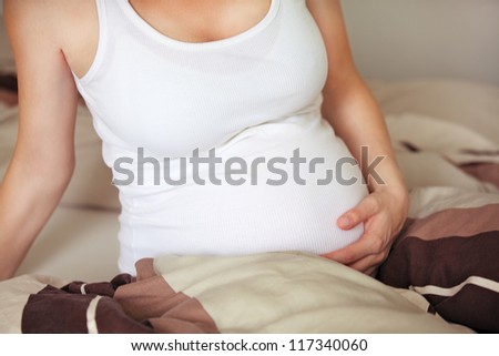 Cropped view of the swollen belly of a pregnant woman sitting in bed crading her abdomen with her hand as she bonds with her unborn child