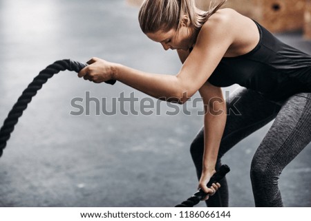 Fit young blonde woman in sportswear working out with ropes during an exercise session in a gym