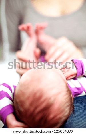 Tiny newborn baby lying on its mothers lap with its head towards the camera with shallow dof