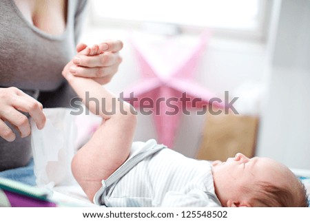 Mother changing a tiny newborn baby\'s nappy as it lies on its back on a changing table in the nursey