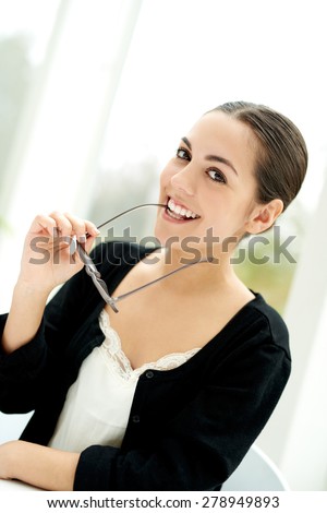 Playful young businesswoman glancing sideways smiling at the camera while holding her eyeglasses in her hand