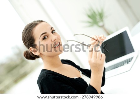 Pretty stylish businesswoman holding her eyeglasses in her hand glancing sideways at the camera with a smile