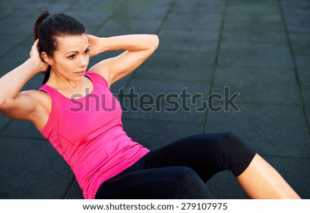 Woman doing situps on the floor outside with hands behind head.