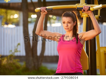 Muscular woman in deep concentration while exercising arms and upper body on a weights machine.