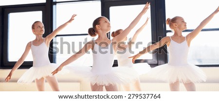 Young ballerinas practicing a choreographed dance all raining their arms in graceful unison during practice at a ballet school
