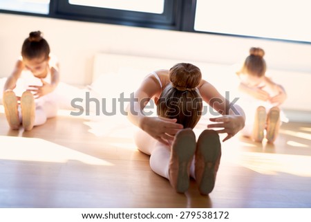 Group of young ballerinas in class doing stretching exercises seated on the wooden floor as they warm up before practice to increase their suppleness