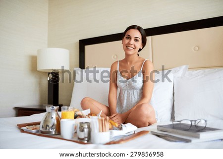 Attractive woman in nightgown relaxing in bed with breakfast tray and pile of books.
