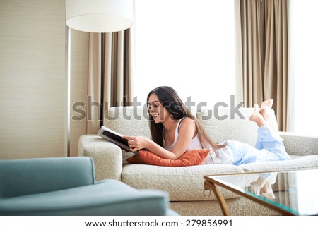 Woman lying on couch with ankles crossed reading a magazine and smiling.