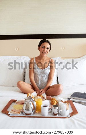Attractive woman in nightgown smiling and relaxing in bed with breakfast tray and books.