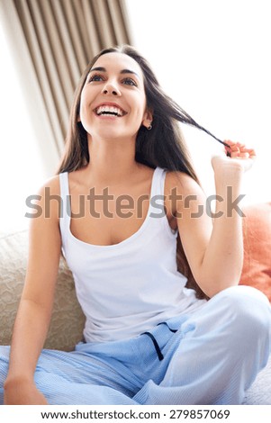 Young woman with head tilted back laughing sitting on couch and playing with hair.