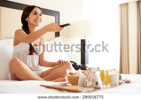 Young woman smiling having breakfast in bed and watching television.