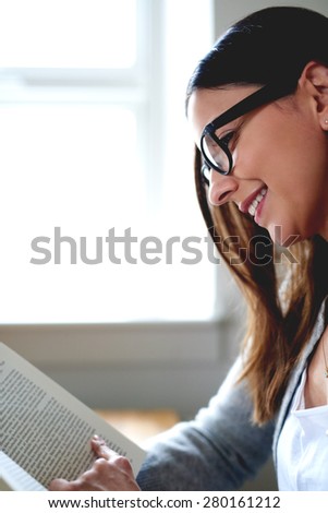 Side view of woman smiling while sitting at desk in home office reading a book.