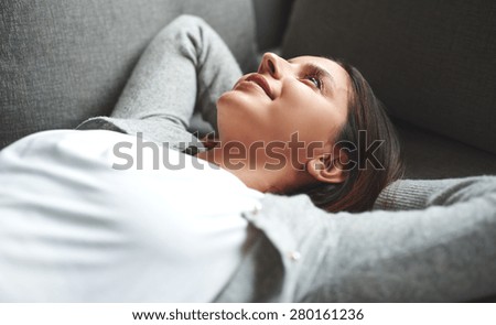 Woman laying on back and relaxing with hands behind her head on couch.