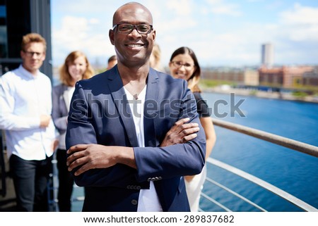 Black male executive standing with arms crossed in front of colleagues