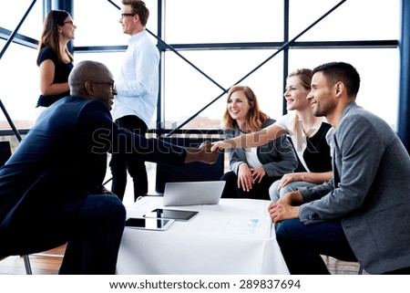 Black male executive sitting and shaking hands with white female colleague