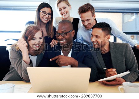 Black male executive smiling at camera with colleagues gathered around him and laptop