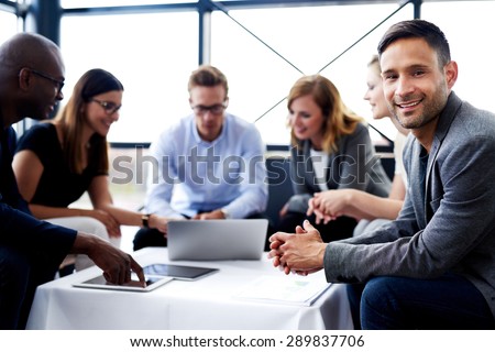 White male executive sitting and smiling at camera during a meeting with colleagues