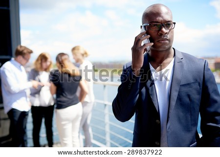 Black male executive on cellphone with colleagues gathered in the background