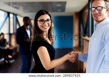 White female and white male executives shaking hands and smiling at camera