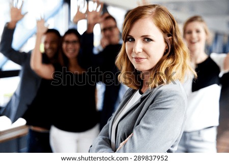 Female white executive standing in front of colleagues with their arms in air