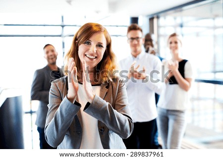 Young white female executive standing in front of colleagues clapping and smiling