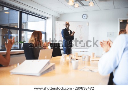 Black male executive standing at head of table in conference room smiling leading meeting
