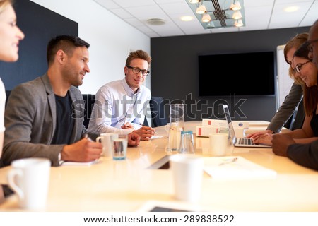 White male executive smiling at camera during a meeting with colleagues