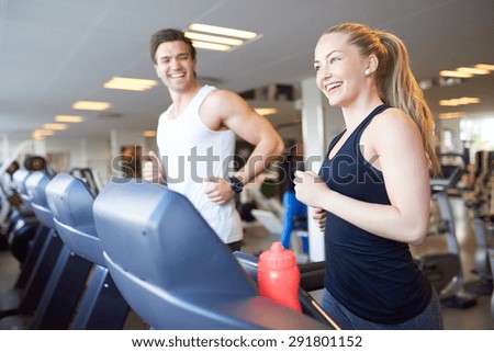 Healthy Young Couple Doing Running Exercise on Treadmill Device Inside the Gym with Happy Facial Expressions.